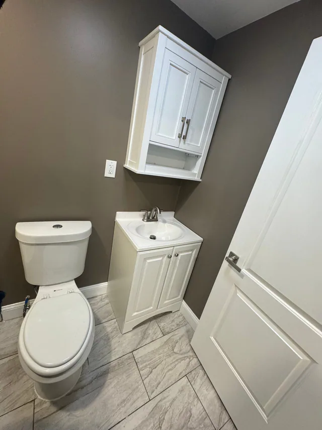 Finished bathroom with warm brown walls, white vanity, wall cabinet over the toilet, and marble-look tile floor